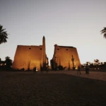 Luxor Temple pylon and obelisk at dusk with palm trees