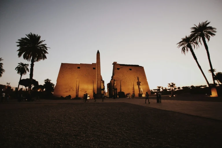 Luxor Temple pylon and obelisk at dusk with palm trees