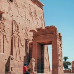 Carved pylon at Philae Temple with a visitor seated by the gate