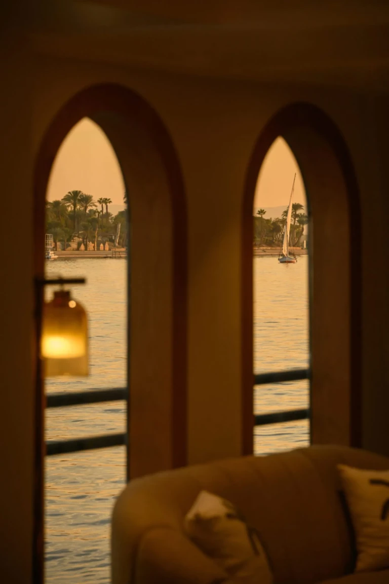 Arched windows framing the Nile and a felucca at sunset on Le Fayan