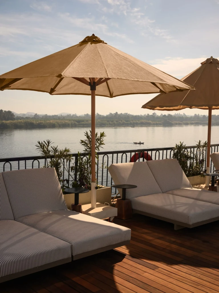 Cushioned sun loungers under parasols facing the Nile on Le Fayan
