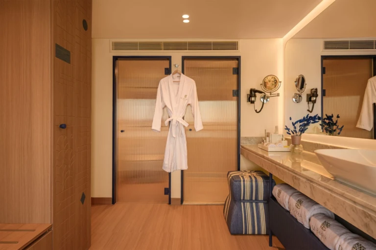 Le Fayan bathroom with bathrobe on door, vanity and blue bench