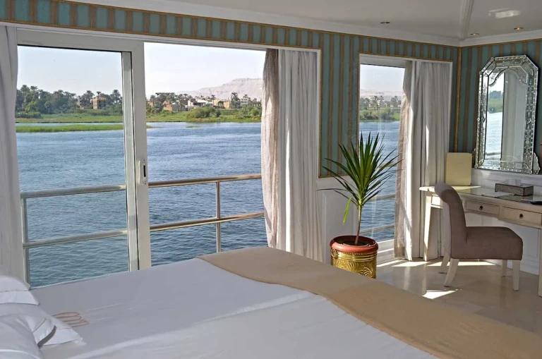Cabin bed facing wide Nile view windows and a palm plant