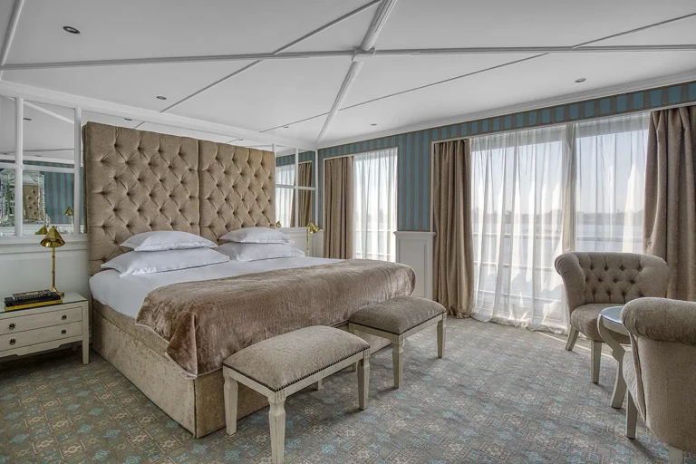 Suite with tufted bed, footstools and armchairs by curtains