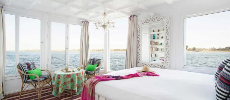 Cabin with bed, small table and armchairs by river windows