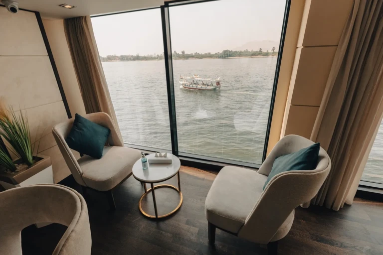 Armchairs facing a panoramic Nile window with a passing boat on the Nebu