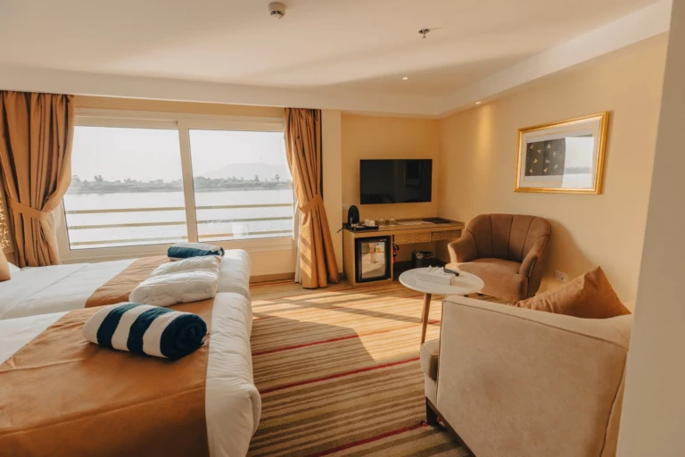 Cabin with bed, armchairs and TV facing a Nile window on the Nebu