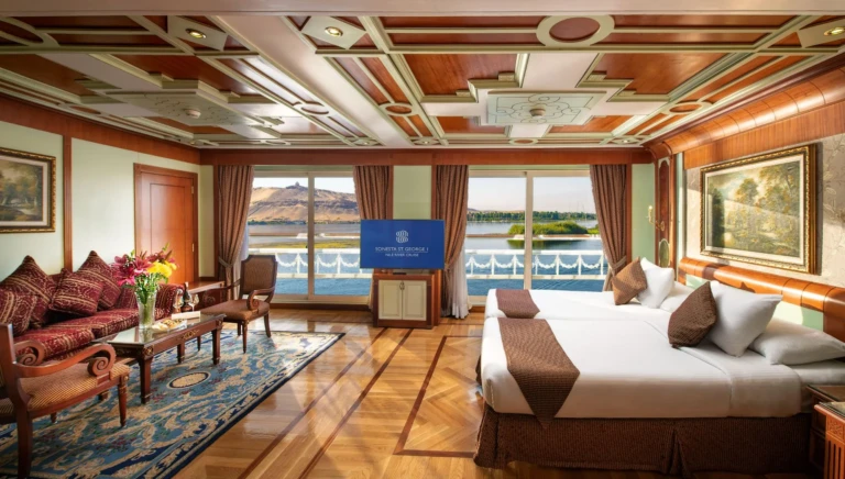 Suite sitting area with red sofa and bed beside river windows