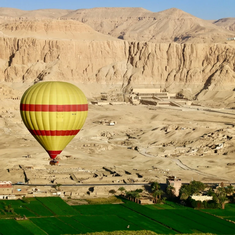 Hot air balloon drifting near Hatshepsut temple and desert cliffs