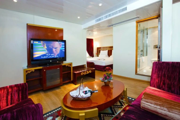 Red armchairs and oval coffee table facing a TV in an Al Hambra suite