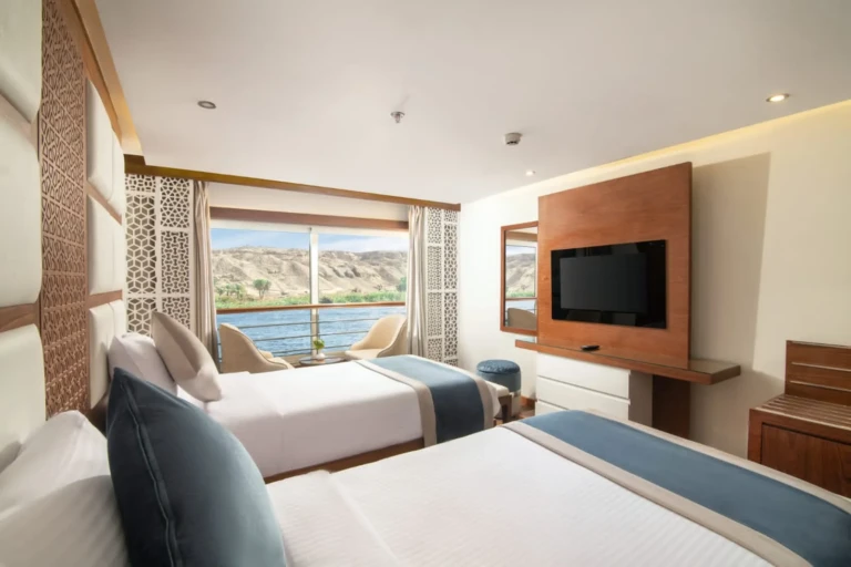 Twin beds facing a river-view window and TV on the Nile Capital