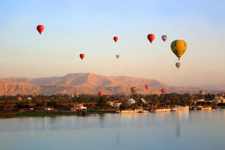 Hot air balloons rising over the Nile and desert hills at dawn