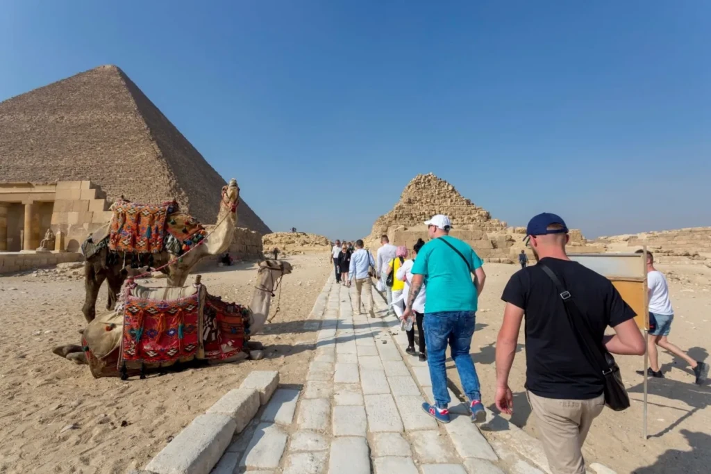 Visitors walking past camels toward the Great Pyramid of Giza