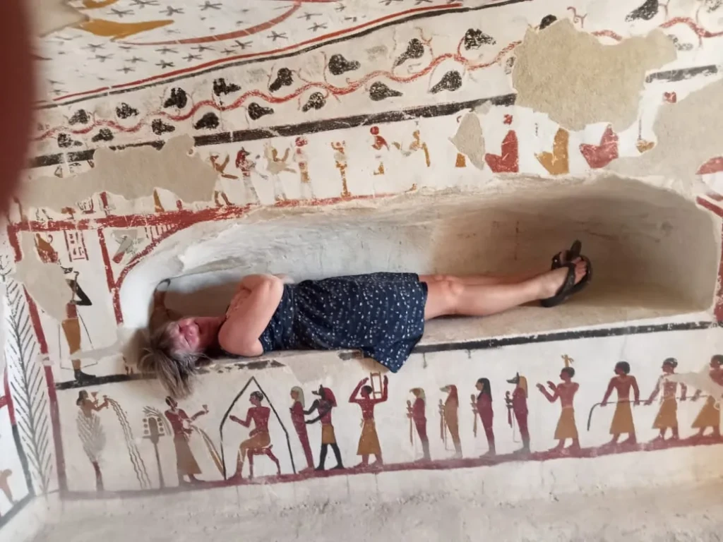 Visitor resting on a bench beneath painted tomb decoration